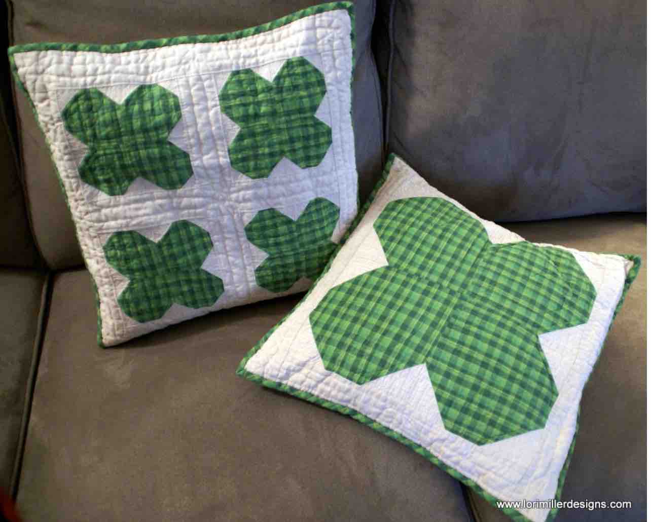 Two square pillows on a couch. One pillow has four quilted shamrocks and the other has one large quilted shamrock.